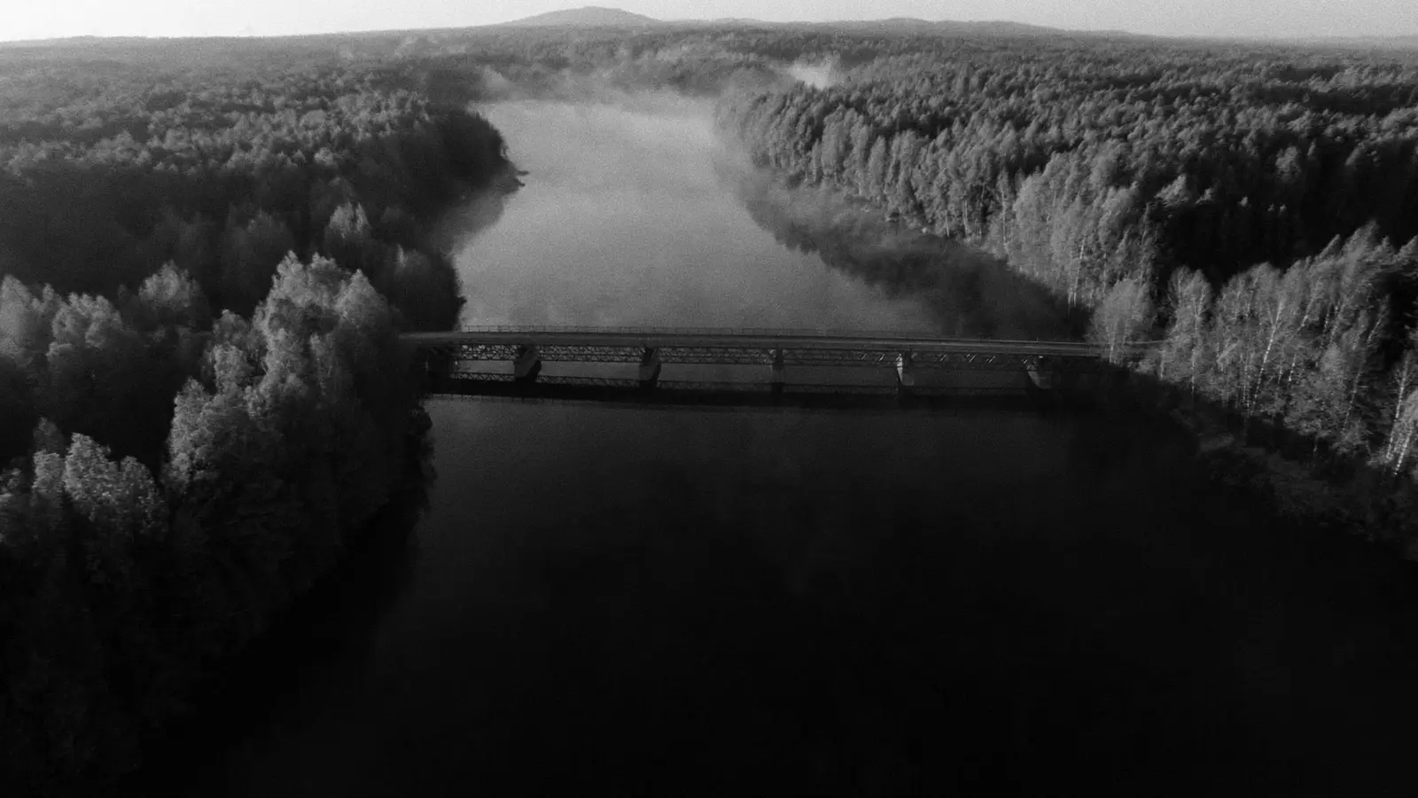 Vue aérienne d'une rivière bordée de forêt, traversée par un pont